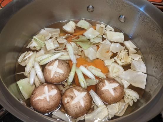 Pot of dashi with cut vegetables - cabbage, scallions, carrots, and mushrooms