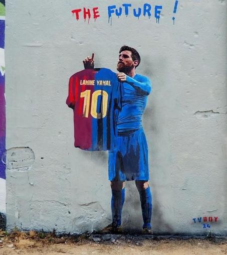 Streetartwall. A paste-up on a gray street wall shows footballer Lionel Messi with a full beard in a blue jersey and shorts. He is holding up a red and blue jersey with the yellow number 10 and the name 
