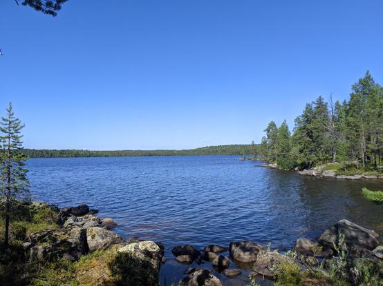 Un lac près d'Inari entouré de rochers et d'arbres. Le ciel est bleu.