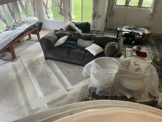 Photo taken from top of stairs down onto concrete slab floor and a jumble of furniture partially covered with plastic sheeting.  