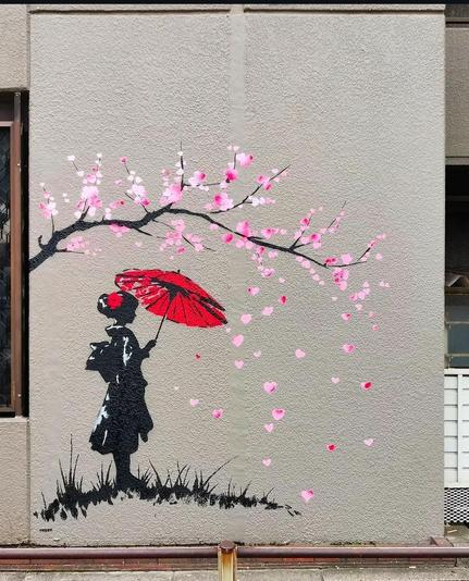 Streetartwall. The enchanting mural of a little geisha under a cherry tree was sprayed on a gray house wall next to an Asian window. The mural is sprayed on with stencils and painted in the main colors black, white, pink and red. It shows the silhouette of a geisha with a red umbrella standing under a bent branch of a cherry tree in the grass. Pink cherry tree blossoms fly through the air in front of her. Simply beautiful.
Info: The works can be seen in Tabby's solo exhibition at the Kawamatsu Galleries in Tokyo and Osaka. Exhibition: Tabby Japan Tour 2024: 