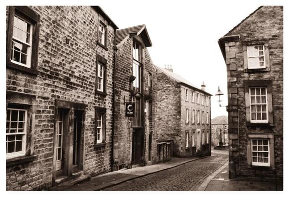 Vintage looking sepia photograph showing an old cobbled street leading down to a market cross.