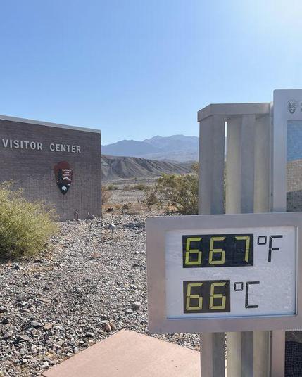 A large digital thermometer displays 667F and 66C in front of a stone building with name Furnace Creek Visitor Center on the side. NPS