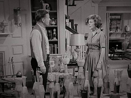 In a scene from Ozzie and Harriet, Harriet gives Ozzie a stern look as they stand next to a primitive wood chess set with two-foot pieces.
