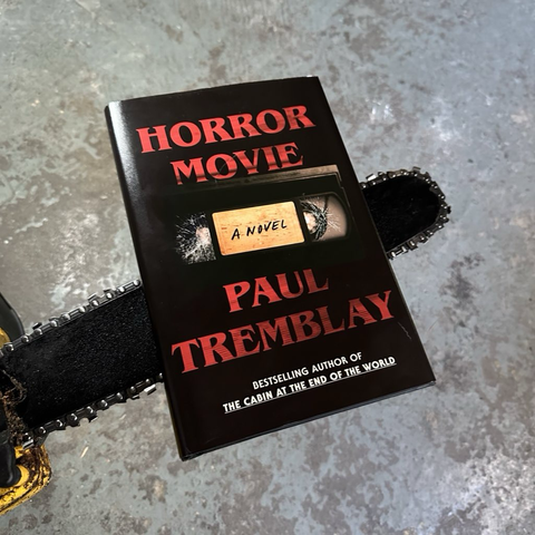 The hardcover book Horror Movie by Paul Tremblay rests on the long blade of a chainsaw.