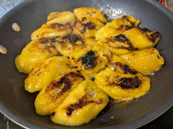 A pan with ripe yellow slices of plantain with blackened spots, all in a frying pan