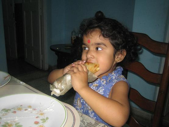 Kid stuffing her mouth with a paratha roll