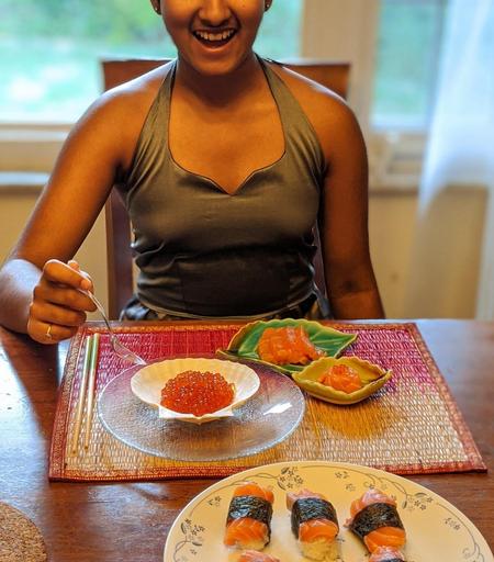 Salmon nigiri (gunkan) and sashimi and ikura in plates in front of a kid seated at a table