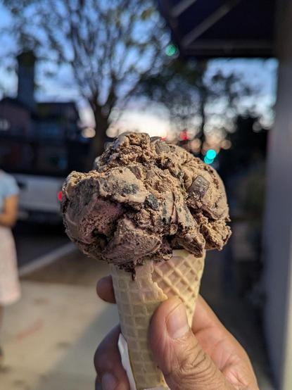 A scoop of chocolate ice cream with chocolate chunks, on a cone