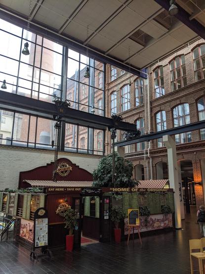 Une galerie commerciale dans une ancienne usine en brique. En haut à gauche une paroi vitrée moderne. En bas, des petits restaurants.