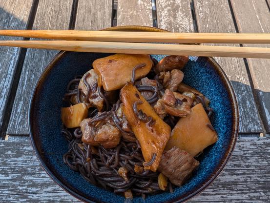 Black rice noodles, mushroom, pork shoulder, hot bean paste in a bowl with chopsticks.
