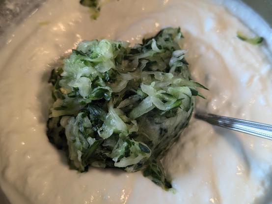 A ball of squeezed salted grated cucumber placed on a bowl filled with garlic yogurt
