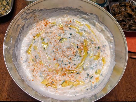 A bowl of touch garlicy cucumber raita or tzatziki, with a drizzle over with olive oil and a sprinkle of smoked paprika