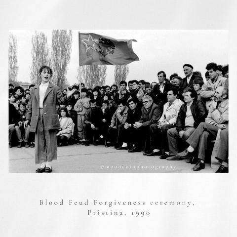 Young girl reciting poetry in front of large group and flag at a Blood Feud Forgiveness Ceremony, Pristina, 1990. Black and White photo, 35mm