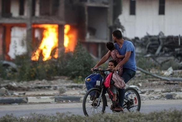 Gaza: father and two children on bicycle ride past burning house