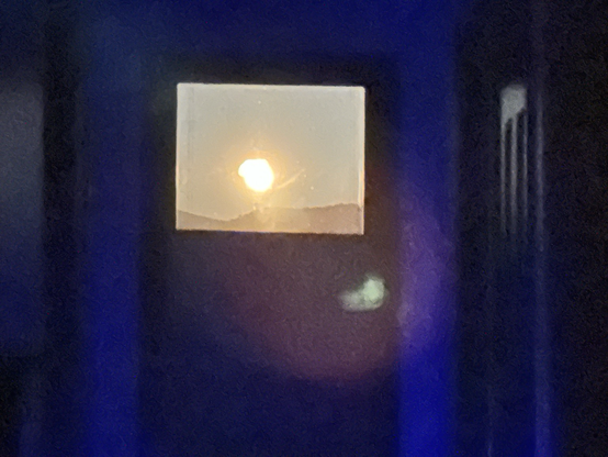 A very blurry attempt at capturing the moon rising over a ridgeline as seen through the top of a glass door at night