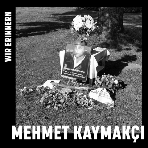 Schwarze Umrahmung, der Text: Wir erinnern Mehmet Kaymakçı. Ein schwarz-weiß-Bild in der Mitte: Ein Foto von Mehmet Kaymakçı auf einer Wiese, darum wurden Blumen abgelegt.
