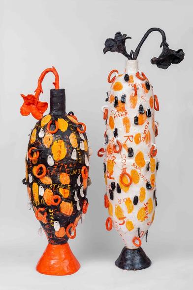 Two abstract ceramic sculptures with slender, oblong vase shapes covered in orange, black, and white decorations with ceramic flowers emerging from the top openings