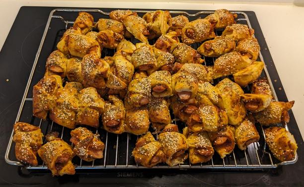 Photo of a big pile of pigs in blankets with yellow orange ish outsides and small sausages peaking out on the side of each.