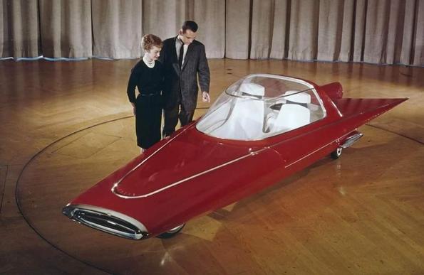 RED pointy car with two people lookin g down at it.
