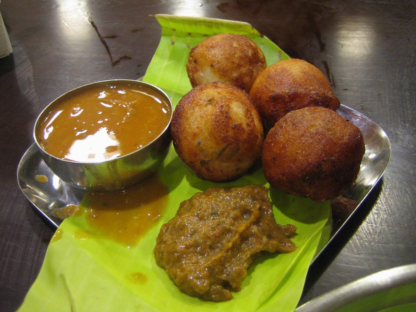 Kuzhi paniyarams - crisp fried brown balls of batter (soft insides) on a plate, with a small bowl of sambar and a large dollop of thick chutney, all on a plate with a banana leaf