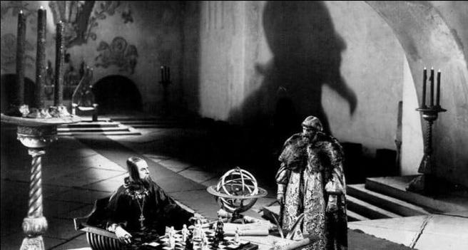 In a scene from Ivan the Terrible Part I, Nikolay Cherkasov sits at a chess board in a large throne room, his face casting a dramatic shadow on the wall.