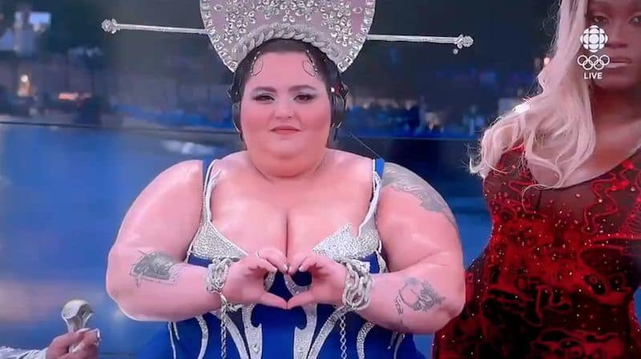 A moment from Paris Olympic Games 2024 opening ceremony.
A big and round woman performer shows the heart or love symbol by touching fingers of her hands