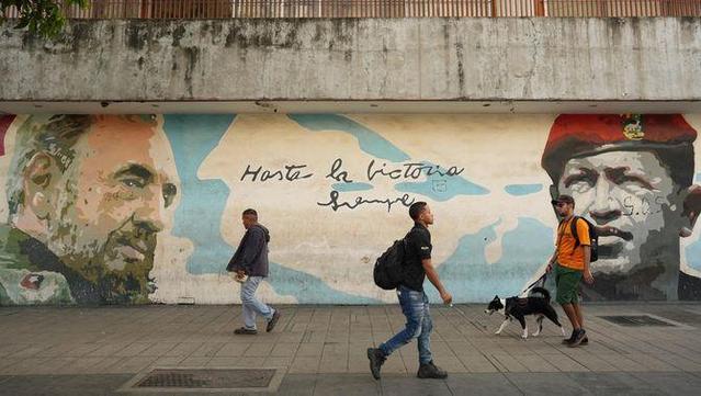 Diversos veneçolans caminen davant d'un mural amb Fidel Castro i Hugo Chávez (Reuters/Alexandre Meneghini)