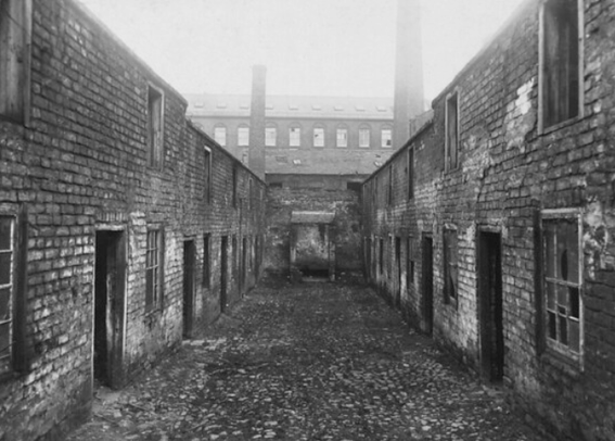 A grim run down view of abandoned houses in a small street in early twentieth Century Belfast. IN the background above the houses is the silhouette of a Mill with two large chimneys. 
A foggy haze hangs over the scene
(Hope's Court pictured in 1912 by AR Hogg - PRONI)