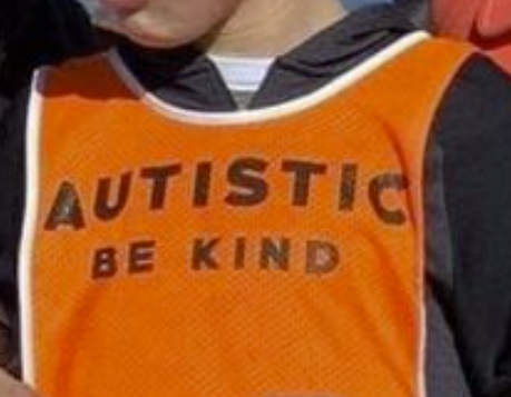 A cropped photo of a tweenage child wearing a bright orange vest with the words 
