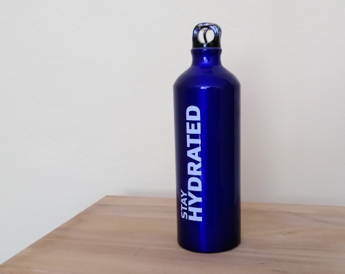 Eine blaue Stahltrinkflasche auf einem Holztisch. Auf der Flasche steht in weißer Schrift 