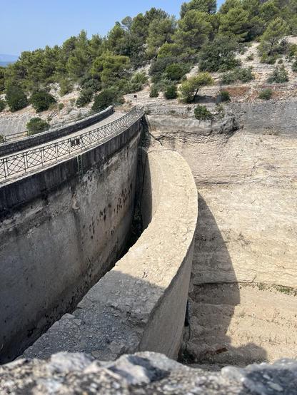 Two walls of a curved dam across a large dry ravine