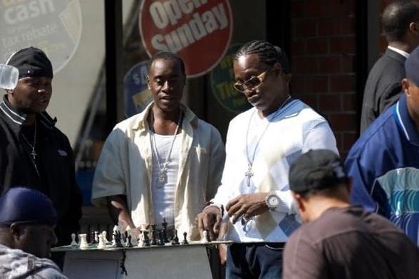 In a scene from Brooklyn's Finest, Wesley Snipes plays chess on a board set up on an outdoor trash can. Don Cheadle watches from the side.