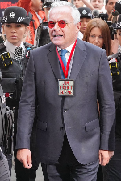 Huw Edwards, escorted to court by police officers, wearing pink-tinted sunglasses on his face and a ‘Jim Fixed It For Me’ badge around his neck