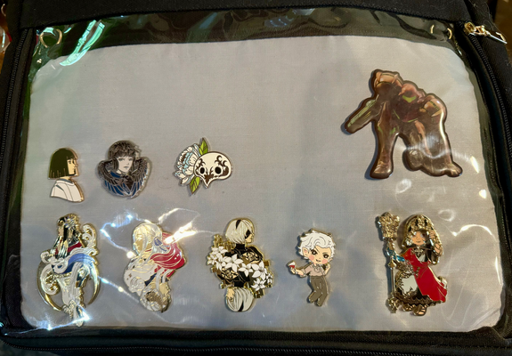 Ita bag with pins depicting Haku (Spirited Away), Meteion (Final Fantasy XIV), an ancient mask (FFXIV), Samus (Metroid), Yotsuyu (FFXIV), Edelgard (Fire Emblem: Three Houses), 2B (Nier Automata), Astarion (Baldur's Gate 3), and the Crystal Exarch (FFXIV).