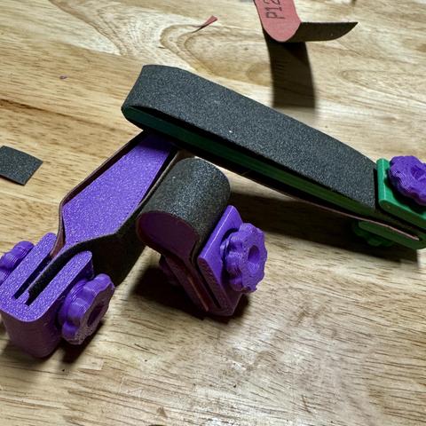 A small, purple and green 3D-printed sanding sticks on a wooden surface.