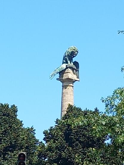 A large column topped with a trapped eagle pinned by a lion