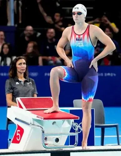World and Olympic Champion Katie Ledecky in the 2024 Olympic Speedo Swimsuit which covers her down to just above her knees.  It's a red white and blue colored swimsuit, and she also is wearing goggles and a swimcap.  The swimsuit says 