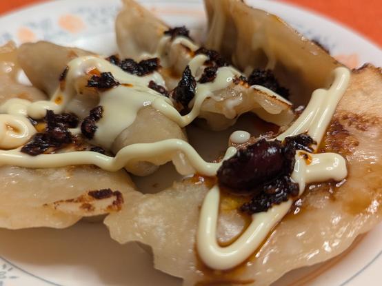 Close up of pan fried gyoza with a swirl of mayonnaise and topped with a bit of chili oil and crisp