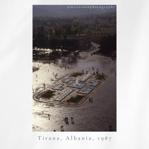 Colour image, muted vintage tones, from a hotel view from high up, main square with fountains, distant view of the city and people walking.