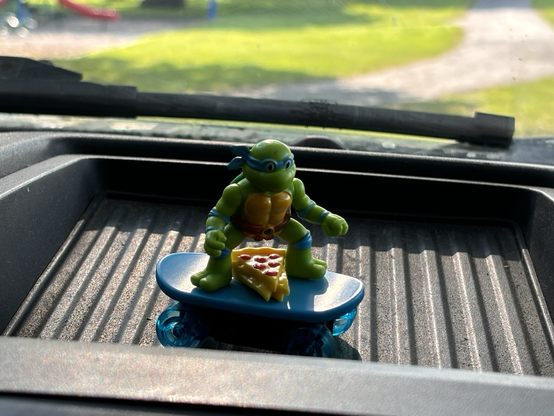 A ninja turtle on a skateboard with pizza on the dash of my work truck
