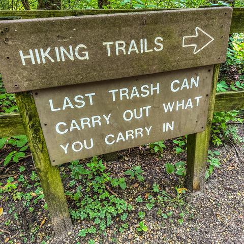 A wooden sign near hiking trails with two messages: 