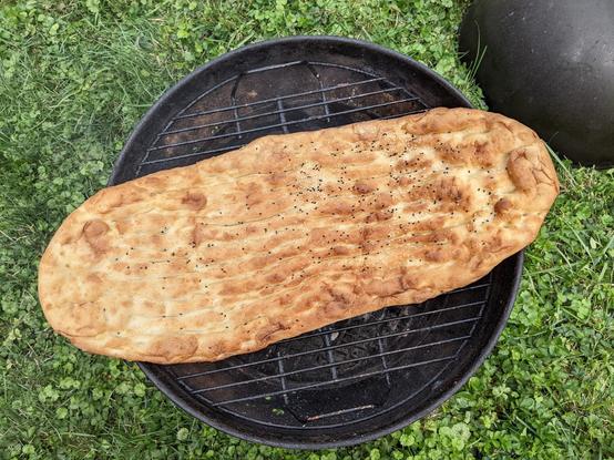 A round grill with an oblong flat bread sprinkled with a bit of white and black sesame seeds on it