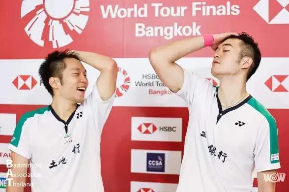 Taiwanese badminton players Lee Yang 李洋 and Wang Chi-lin 網麒麟 at the HSBC Badminton World Tour Finals in Bangkok in front of a sponsor wall. The two are posing with their arms raised to brush their hair backward as if they are pop idols.