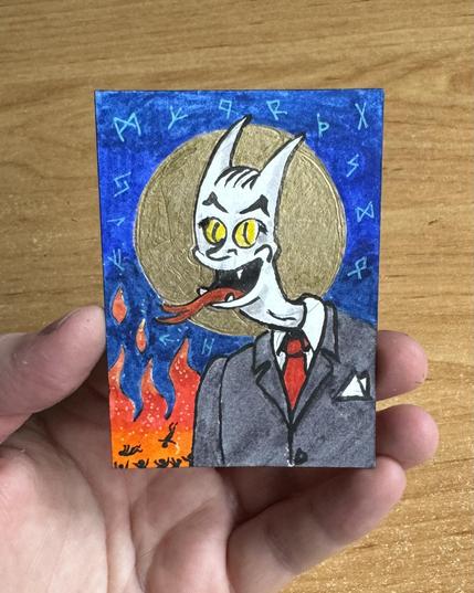 A cartoonish devil-like character is depicted wearing a suit and tie, holding its tongue out, with flames and runes in the background. The drawing is held by a hand against a wooden surface.