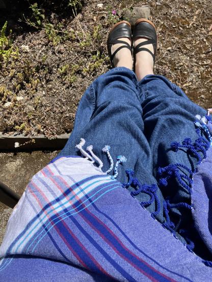 Camera angle looks down at my lap and feet showing a blue and white kikoi wrap over blue bubble pants, and my black ballet-style shoes.