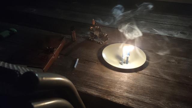 Two lit candles on a platter, sitting on top of a table. An incense burner is sitting off to the side with smoke wafting towards them. An odd form is seen within the smoke, a figure or some such.