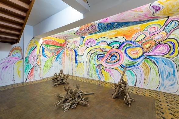 Gallery with walls drawn all over with colorful, semi-abstract motifs. On the floor are abstract wooden sculptures 