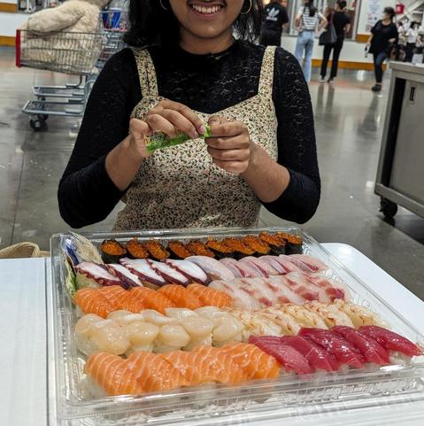 Kid with a big smile tearing open a wasabi packet with a big tray of sushi in front.