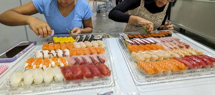 Two kids with trays of sushi in front of them